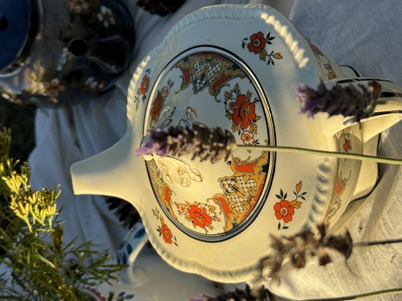 Tetera antigua de porcelana blanca con flores naranjas, entre espigas de lavanda